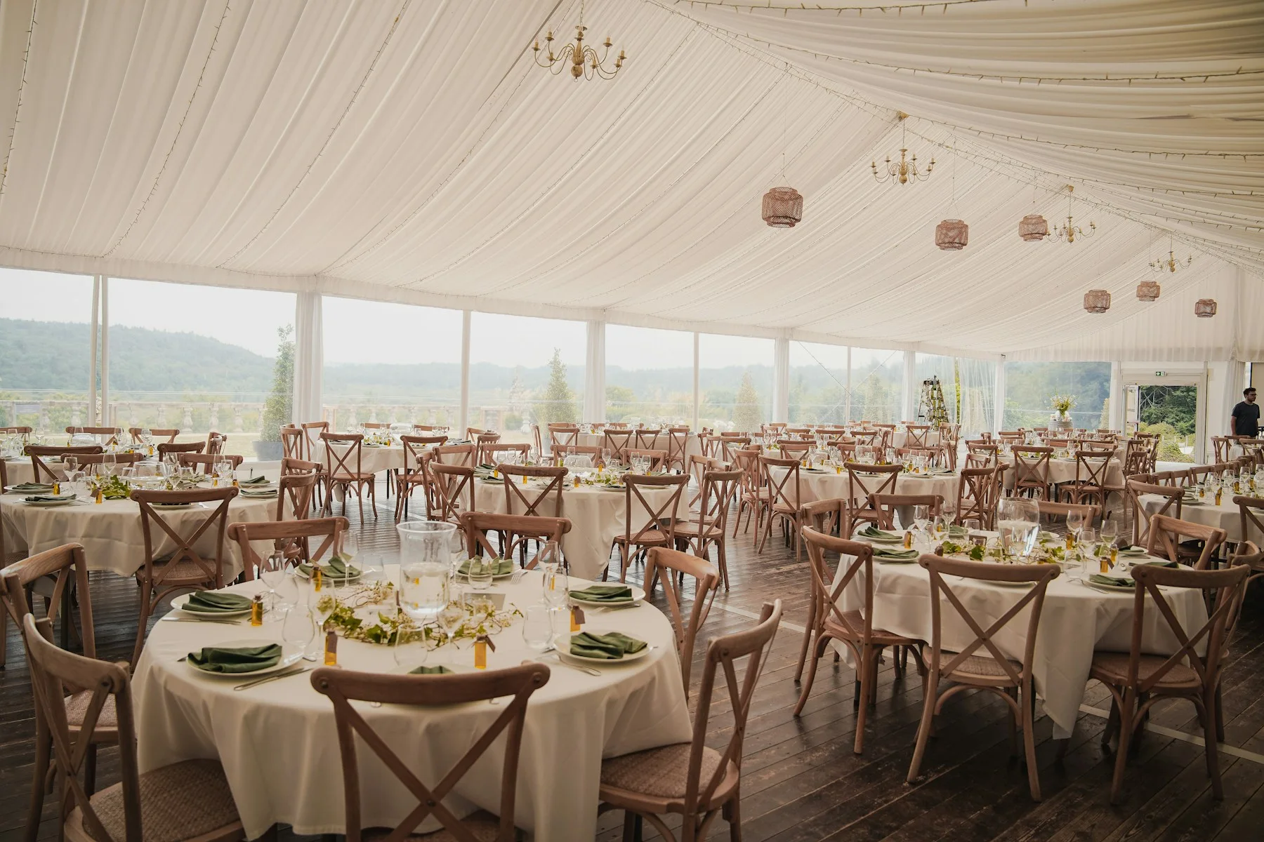 Elegant white-lined marquee interior with round dining tables, wooden chairs and hanging lights